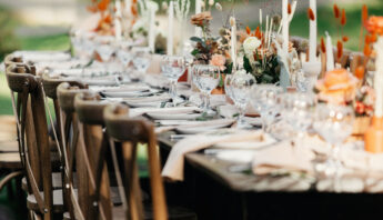 Boho wedding table for guests at bouquet after wedding ceremony and photo for marriage blog about interior. Candles, bouquets, napkins, dishes, accessories and glasses on table with chairs, outdoors